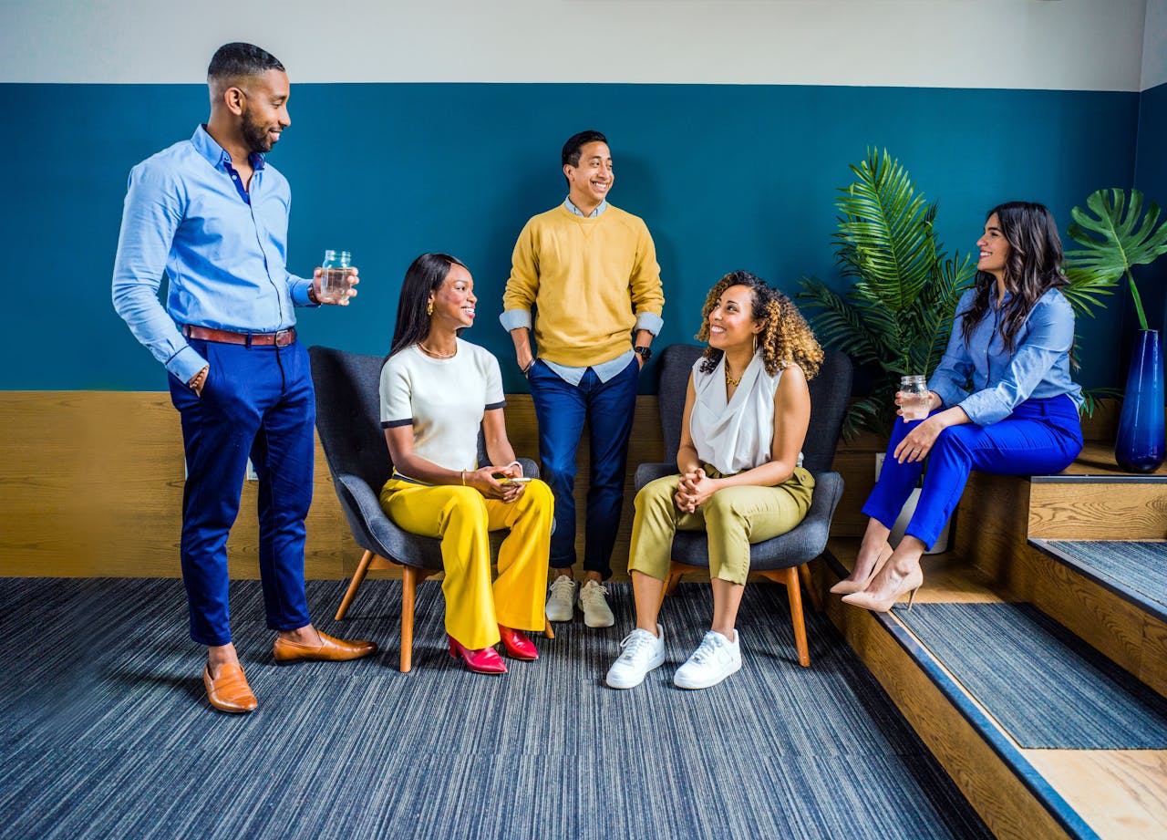 services-03 A diverse group of five professionals engaging in a casual indoor meeting, smiling and talking.