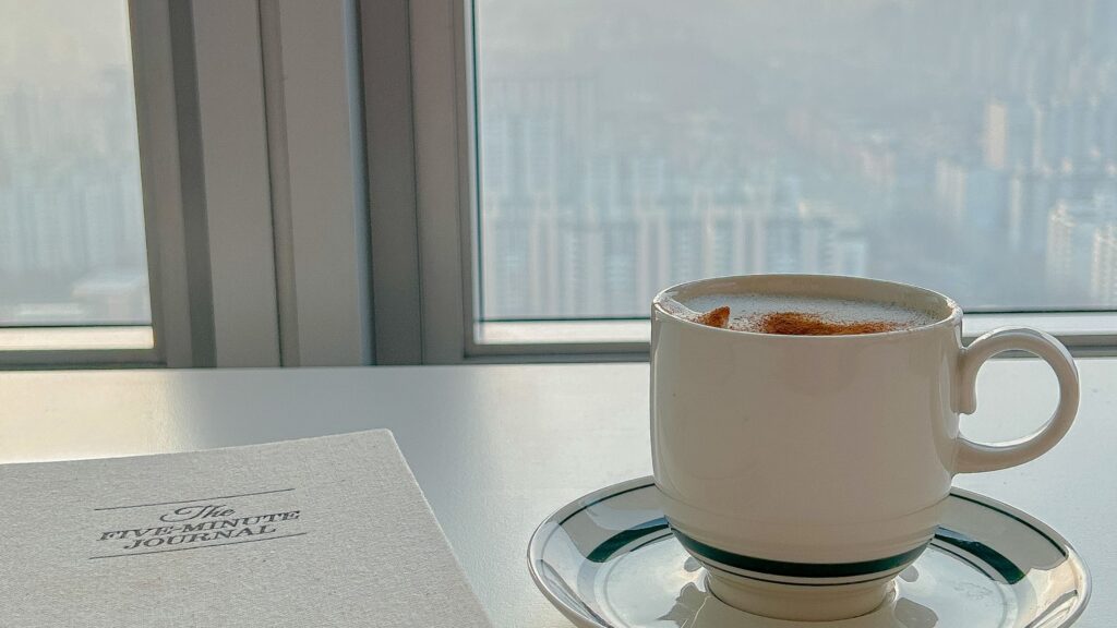 mug and gratitude journal on table in front of a modern apartment door